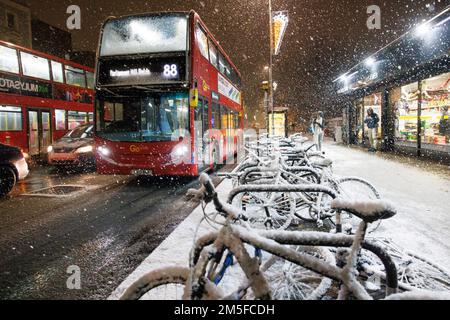 Vor der U-Bahn-Station Stockwell fällt Schnee auf Fahrrädern, während ein Londoner Bus in Stockwell, Südwest-London, als unvorhergesehener kalter sn vorbeifährt Stockfoto