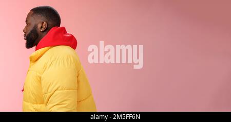 Profil Studio erschossen bärtigen jungen 25s afrikanischen Kerl in gelb Jacke rot Kapuzenpullover Look links normal unbeschwert entspannten Ausdruck stehen Warteschlangenreihenfolge Stockfoto