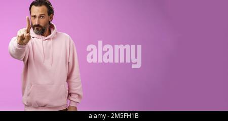Eine Regel hören. Serious-looking herrisch fokussiert bestimmt erwachsenen bärtigen Mann in rosa Kapuzenpullover verlängern Zeigefinger erste Zahl Schelten Aussage machen Stockfoto