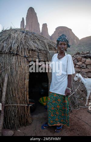 Peul Woman vor einer Strohhütte mit Hintergrundblick auf das Monument Valley von Mali mit der Main de Fatima Felsformation in der Nähe von Hombori Stockfoto