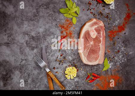 Auf dunklem Hintergrund werden rohe Schweinekoteletts mit Gewürzen und einer Gabel angeordnet. Stockfoto