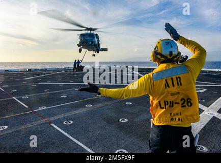 PACIFIC OCEAN (15. März 2022) Aviation Boatswain’s Mate 3. Class Kyro Lee, aus Miami, dem Amphibienschiff USS John P. Murtha (LPD 26) zugewiesen; Leitet einen MH-60s Seahawk-Hubschrauber, der an den „Easy Riders“ des Helicopter Maritime Strike Squadron (HSM) 37 befestigt ist, während einer vertikalen Auffüllung auf See (VERTREP) vom März 15 in Position. John P. Murtha führt gerade Routineeinsätze in der US-3.-Flotte durch. Stockfoto