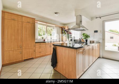 Eine Küche mit Holzschränken und schwarzen Ablageflächen auf der Insel vor der Herdhaube, die von der Decke hängt Stockfoto