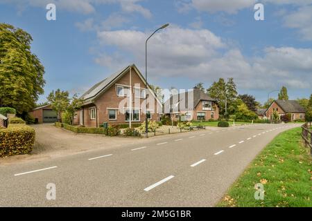 Eine Straße mit Häusern im Hintergrund und Bäumen auf beiden Seiten, entlang einer leeren Straße, die zu einem Parkplatz führt Stockfoto