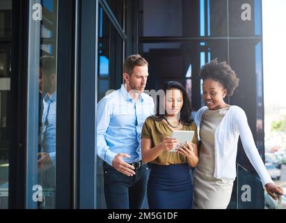 Die Aktienmärkte im Auge behalten. Eine Gruppe von Geschäftsleuten, die ein digitales Tablet benutzen, während sie auf einem Balkon stehen. Stockfoto