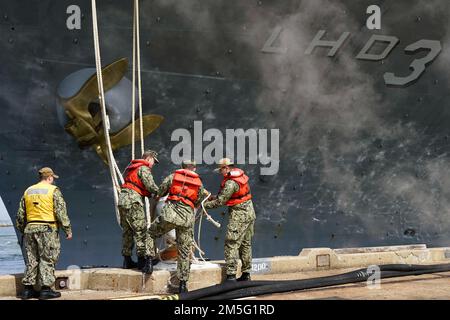 NORFOLK, VA (16. März 2022) - Seeleute entfernen die Anlegestellen vom Pier, während sich das Amphibienschiff USS Kearsarge (LHD 3) der Wasp-Klasse auf den Abflug von der Naval Station Norfolk am 16. März 2022 vorbereitet. Die Kearsarge Amphibious Readiness Group (ARG) hat 22. Marineexpeditionstruppe (MEU) für einen regelmäßig geplanten Einsatz von der Marinestützstelle Norfolk und Camp Lejeune, North Carolina, in die Offensive geschickt. Stockfoto