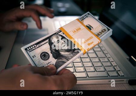 10000 Dollar Banknoten auf einer Laptop-Tastatur. Konzept des Verdienens Geld online, verdienen mit dem Internet, passives Einkommen. Geld verdienen im Internet Stockfoto
