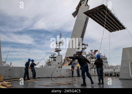 220316-N-PC065-1400 ATLANTISCHER OZEAN – Seeleute, die dem Amphibienschiff USS Arlington (LPD 24) der Klasse San Antonio zugewiesen sind, stabilisieren die Stirn beim Anheben auf das Schiff vor dem Einsatz am 16. März 2022. Arlington ist im Atlantischen Ozean tätig, um Marineeinsätze zu unterstützen, um die Stabilität und Sicherheit der Meere zu erhalten, um den Zugang zu gewährleisten, Aggressionen abzuwehren und die Interessen der US-Verbündeten und Partner zu verteidigen. Stockfoto