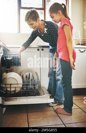 Diese Maschine macht uns das Leben leichter. Eine fröhliche Mutter und Tochter, die zu Hause zusammen Geschirr spülen. Stockfoto