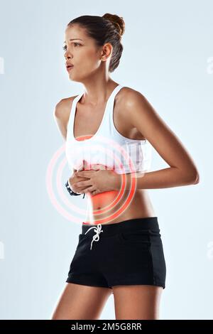 Ihr Magen ist verknotet. Studioaufnahme einer sportlichen jungen Frau, die ihren Magen vor grauem Hintergrund in Schmerzen hält. Stockfoto