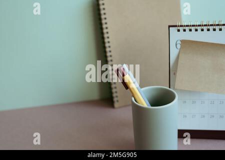 Notizbuch- und Bleistifthalter, Kalender, Notizblock auf dem Schreibtisch. Mintfarbener Wandhintergrund. Arbeitsplatz, Neujahrsplan, Geschäft, Bürobedarf Stockfoto