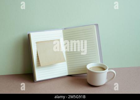 Offenes Notizbuch, Haftnotizen und eine Tasse Kaffee auf dem Schreibtisch. Mintfarbener Wandhintergrund. Arbeitsplatz, Geschäft, Studienplatz Stockfoto