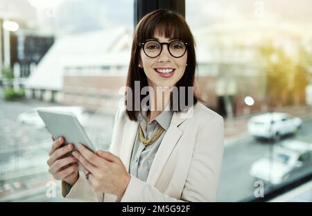 Keine Sorge, ich habe das hier. Porträt einer jungen Geschäftsfrau, die ein digitales Tablet benutzt, während sie im Büro steht. Stockfoto