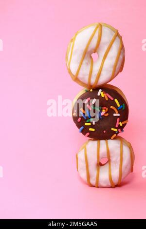 verity Mini-Donuts mit Glasur und Prise auf rosa Hintergrund Stockfoto