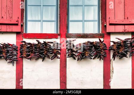 Chili-Paprika, zum Trocknen an der Fassade hängende Espelette, typisches Fenster mit roten Fensterläden, Details, Espelette, Departement Pyrenees-Atlantiques. Stockfoto