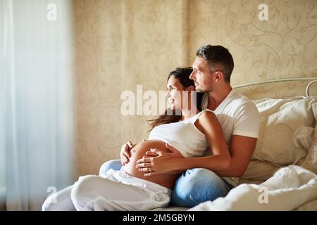Einen Moment miteinander verbringen. Ein Mann und eine schwangere Frau sitzen zusammen in einem Schlafzimmer. Stockfoto