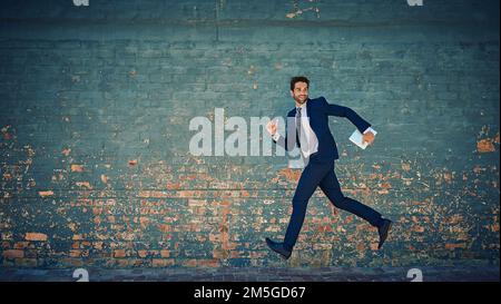 Er rast auf seine Ziele zu. Ein junger Geschäftsmann, der mitten in der Luft gegen eine Ziegelmauer springt. Stockfoto