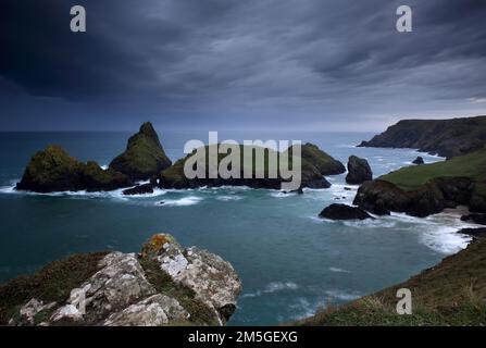 Dramatische Wolken an der felsigen Küste, aufsteigender Regenschauer über felsigen Inseln mit schäumender Brandung, Kynance Cove, The Lizard, Cornwall, England, Großbritannien Stockfoto