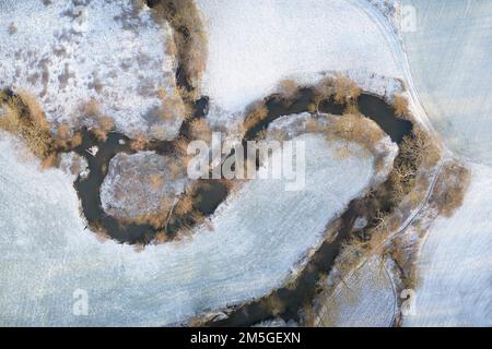 Gewundene Flussstrecke durch schneebedeckte Wiesen im Winter von oben, Drohnenfotografie, Bayern, Deutschland Stockfoto