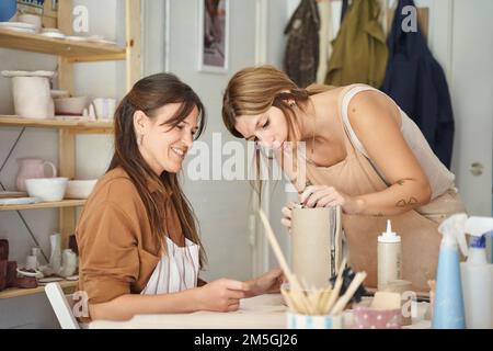 Eine Frau, die einer Schülerin mit Kunsthandwerk in einem Töpferkurs hilft. Handwerk, Kunst und Hobbys. Stockfoto