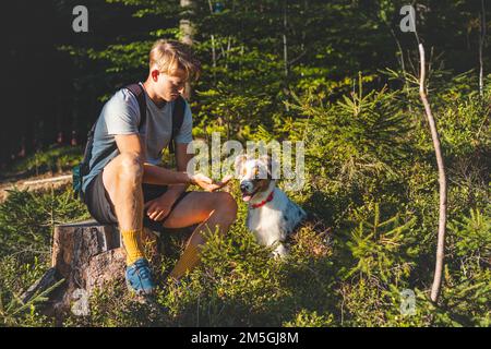 Ein ehrliches Porträt eines Meisters, der seinen australischen Schäferhund auf einem Spaziergang im Wald fütterte. Verbindung zwischen Hund und Mensch. Er füttert seine geliebten vier-l. Stockfoto