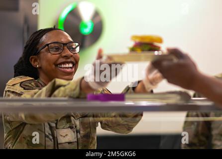 USA Air Force Airman 1. Class Tommiesha Bailey, 509. Force Support Squadron Sustainment Services Specialist übergibt einem Airmen auf dem Whiteman Air Force Base, Missouri, 17. März 2022 ein frisch zubereitetes Essen. Spezialisten für Nachhaltigkeit sind für den Betrieb des Speisesaals verantwortlich, vom Kochen aller Mahlzeiten bis hin zur Sicherstellung eines ausgewogenen Menüs. Stockfoto