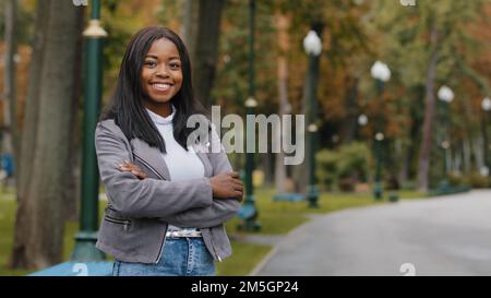 Porträt im Freien eine ethnische Geschäftsfrau, die mit weißen Zähnen auf die Kamera schaut und ein Lächeln in der Zahnheilkunde entwickelt. Afroamerikanisches Mädchen lächelnd Frau im Stehen Stockfoto