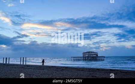 Brighton UK 29. Dezember 2022 - Ein Wanderer am Brighton Beach geht am West Pier vorbei, während die Sonne an einem glühenden, hellen Morgen entlang der Südküste aufgeht. : Credit Simon Dack / Alamy Live News Stockfoto