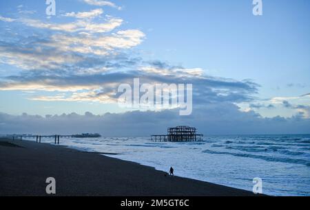 Brighton UK, 29. Dezember 2022 - Ein Hundefreund am Brighton Beach geht am West Pier vorbei, während die Sonne an einem glühenden, hellen Morgen an der Südküste aufgeht. : Credit Simon Dack / Alamy Live News Stockfoto