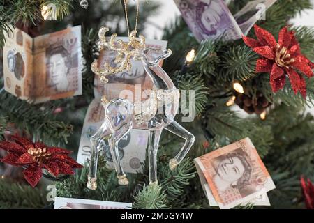 Weihnachtsbaum mit 10 Pfund und 20 Pfund Noten als Dekoration mit einem Glas und goldenen Rentier im Vordergrund, teure Weihnachten Stockfoto