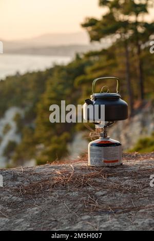 Kleiner, alter Wasserkocher auf einem Lagerfeuer auf einer Bergwiese bei schlechtem Wetter. Kaffee oder Tee am Kamin machen. Reisen Sie in die Berge. Stockfoto