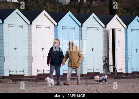 Die Leute gehen vorbei an Strandhütten am Avon Beach in Mudeford, Dorset. Foto: Donnerstag, 29. Dezember 2022. Stockfoto