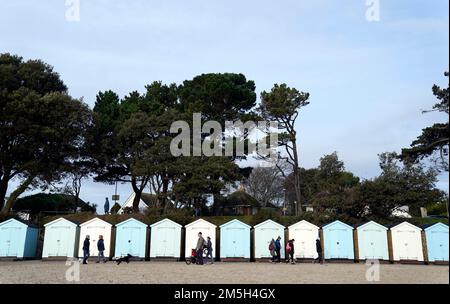 Die Leute gehen vorbei an Strandhütten am Avon Beach in Mudeford, Dorset. Foto: Donnerstag, 29. Dezember 2022. Stockfoto