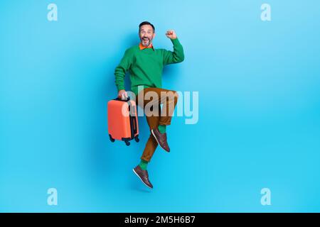 Großes Foto eines erwachsenen, attraktiven Mannes, der springt, hebt die Faust. Tragen Sie trendige grüne Kleidung, isoliert auf blauem Hintergrund Stockfoto