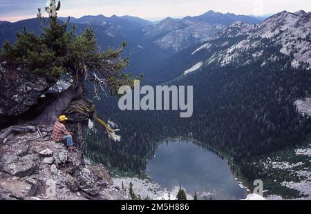 International Selkirk Loop - Römische Seen in der Nähe der Bonners Ferry. Ein Wanderer macht eine Pause auf einer hohen Klippe mit Blick auf die römischen Seen. Hohe Bergseen in den herrlichen Selkirk Mountains, die römischen Seen sind ein großartiger Ort für Wanderungen, Picknicks und rustikales Camping. Bonners Ferry, Idaho (48,630° N 116,593° W) Stockfoto