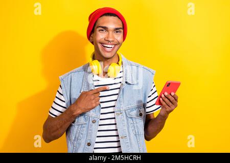 Foto eines positiven lustigen Benutzers, der trendige Kleidung trägt und das Gerät für das iphone samsung App isoliert auf gelbem Hintergrund wirbt Stockfoto