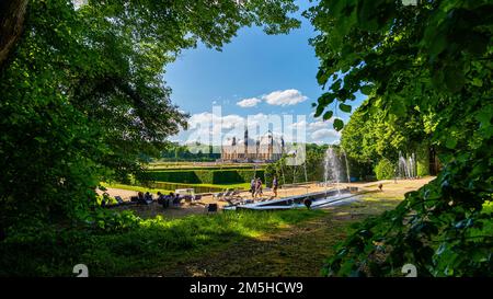 Maincy, Frankreich - 21. Mai 2022: Blick von Bäumen auf Besucher, die sich in einem klassischen französischen Garten (Vaux-le-Vicomte) ausruhen und spazieren. Foto aufgenommen Stockfoto