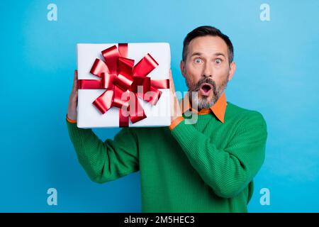 Das Foto des erwachsenen netten Mister beeindruckt schockiertes weihnachtsgeschenk tragen trendiges grünes Kleidungsstück isoliert auf blauem Hintergrund Stockfoto