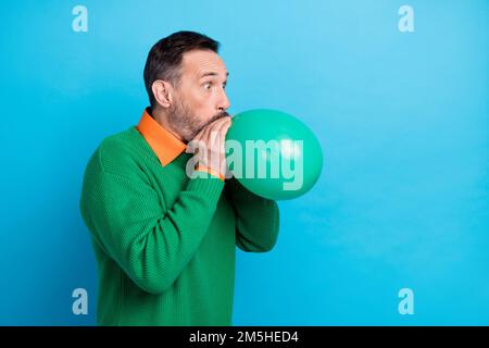 Fotoportrait des reifen, netten Mister Blow Luftballon Feiertage tragen Sie trendige grüne Kleidung isoliert auf blauem Hintergrund Stockfoto