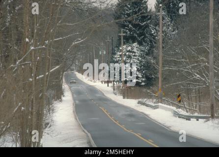 Ohio & Erie Canalway - Byway im Winter in der Nähe der Boston Mills Road. Ein Auto fährt auf dieser einsamen Straße durch die grünen, schneebedeckten Bäume in der Nähe des Ohio & Erie Canalway. Standort: Ohio (41,260° N 81,566° W) Stockfoto