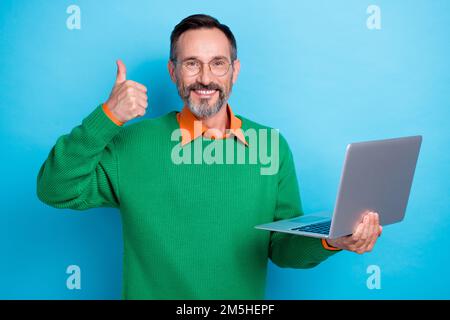 Foto eines erwachsenen, netten Mister, der ein Notebook hält, das ein Lächeln zeigt Tragen Sie trendiges grünes Kleidungsstück isoliert auf blauem Hintergrund Stockfoto