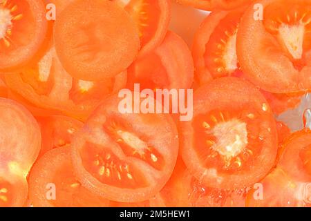 Nahaufnahme frischer Tomatenscheiben auf weißem Hintergrund. Tomatenscheiben in sprudelndem Wasser auf weißem Hintergrund, Nahaufnahme. Horizontales Bild Stockfoto