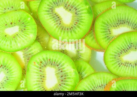 Nahaufnahme von Kiwis in Flüssigkeit mit Blasen. Scheiben von grünen, reifen Kiwis im Wasser. Nahaufnahme frischer Scheiben grüner Kiwis auf weißem Hintergrund Stockfoto