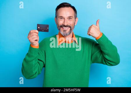 Fotoporträt eines erwachsenen, netten Mister Hold zeigt Daumen hoch gute Arbeit angezogen stilvolle grüne Kleidung isoliert auf blauem Hintergrund Stockfoto