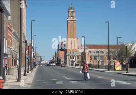 Ohio & Erie Canalway - Lonely Street in Cleveland. Ein Mann überquert die Straße in der Westside Market Gegend von Cleveland. Im Hintergrund befindet sich ein großes orangefarbenes Gebäude mit einem hohen Glockenturm. Standort: Cleveland, Ohio (41,485° N 81,703° W) Stockfoto