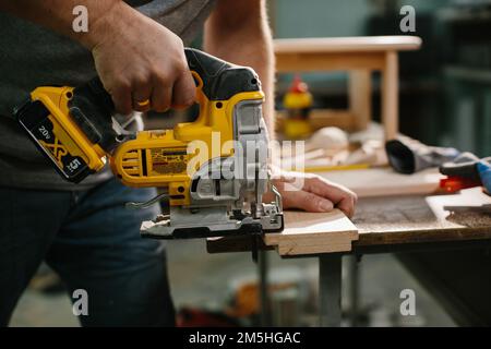 Ein Holzarbeiter, der mit einer Stichsäge eine Krümmung in ein Werkstück aus Kiefer schneidet. Stockfoto