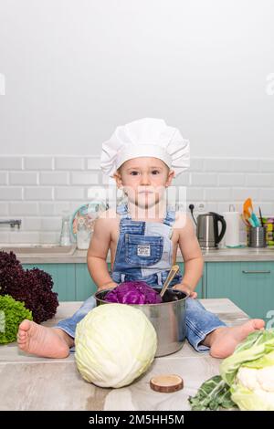 Ein süßer kleiner Junge im Koch-Kostüm kocht mit Emotionen. Hochwertiges Foto Stockfoto