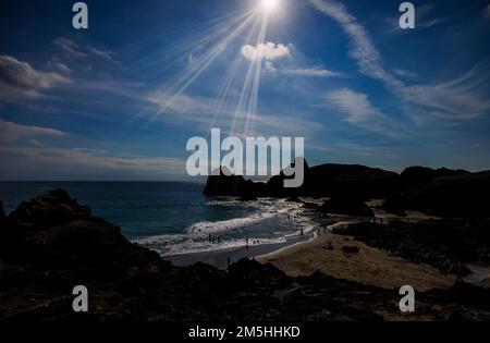 Blick auf die Nachmittagssonne über dem Strand und die silhouettierten Klippen am Kynance Cove auf der Lizard-Halbinsel an der Südküste von Cornwall, Südwestengland Stockfoto