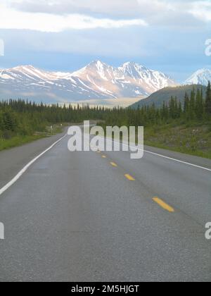 Der George Parks Highway Scenic Byway, der sich entlang des George Parks Highway schlängelt. Die wunderschönen schneebedeckten Berge sind in der Ferne zu sehen, während sich der Parks Highway zwischen üppigen grünen Wäldern schlängelt. Standort: Alaska Stockfoto