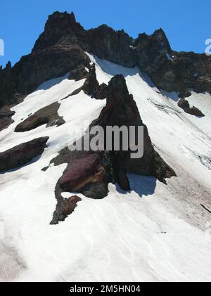 Cascade Lakes Scenic Byway – Gletscher und Gipfel der Cascade Mountains. Dunkle Felsgipfel kontrastieren mit weißen Schneefeldern, die sich an den höheren Gebieten des Broken Top Mountain festkleben. Standort: Oregon (43,525° N 122,148° W) Stockfoto